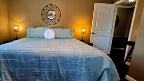 A bedroom with a bed, two bedside lamps, a wall mirror, and a door.