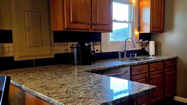 A kitchen with granite countertops, wooden cabinets, a window, and a coffee maker.