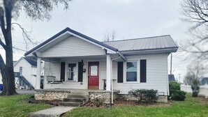 A single-story house with a red front door, a porch with a bench, and a stone foundation.