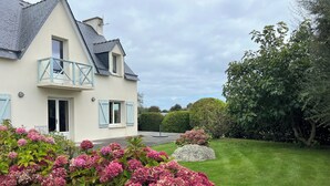 Een tweelaags huis met een balkon, een verzorgd gazon en roze hortensiaplanten.