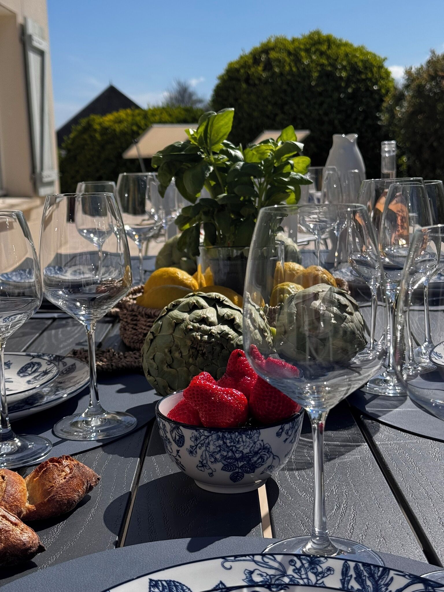 Ulkokattauksessa on pöytä, jonka päällä on viinilaseja, kulho mansikoita, artisokkia ja leipää.