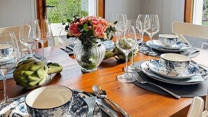 Een eettafel gedekt met blauw-wit bloemdesservies, een vaas met roze bloemen en een artisjok.