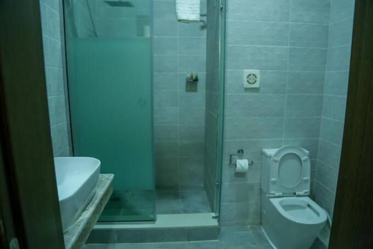Une petite salle de bain carrelée, dotée d’une douche à parois de verre, de toilettes et d’un lavabo.