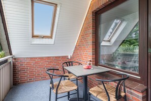 Eine kleine Terrasse im Freien mit Tisch und Stühlen, einem Fenster und einer Ziegelwand.