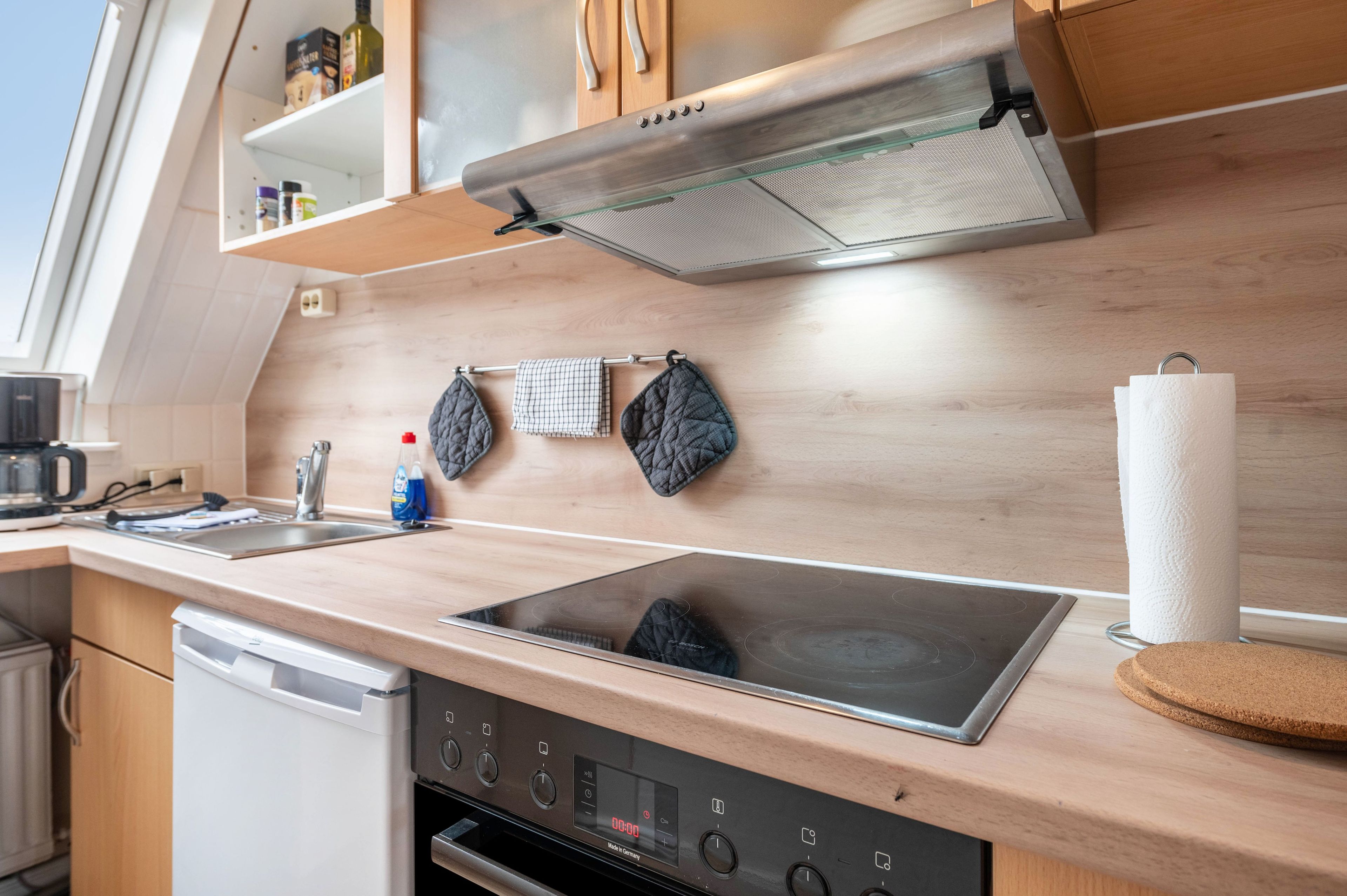 A modern kitchen with a built-in oven, a stainless steel range hood, and a wooden countertop.