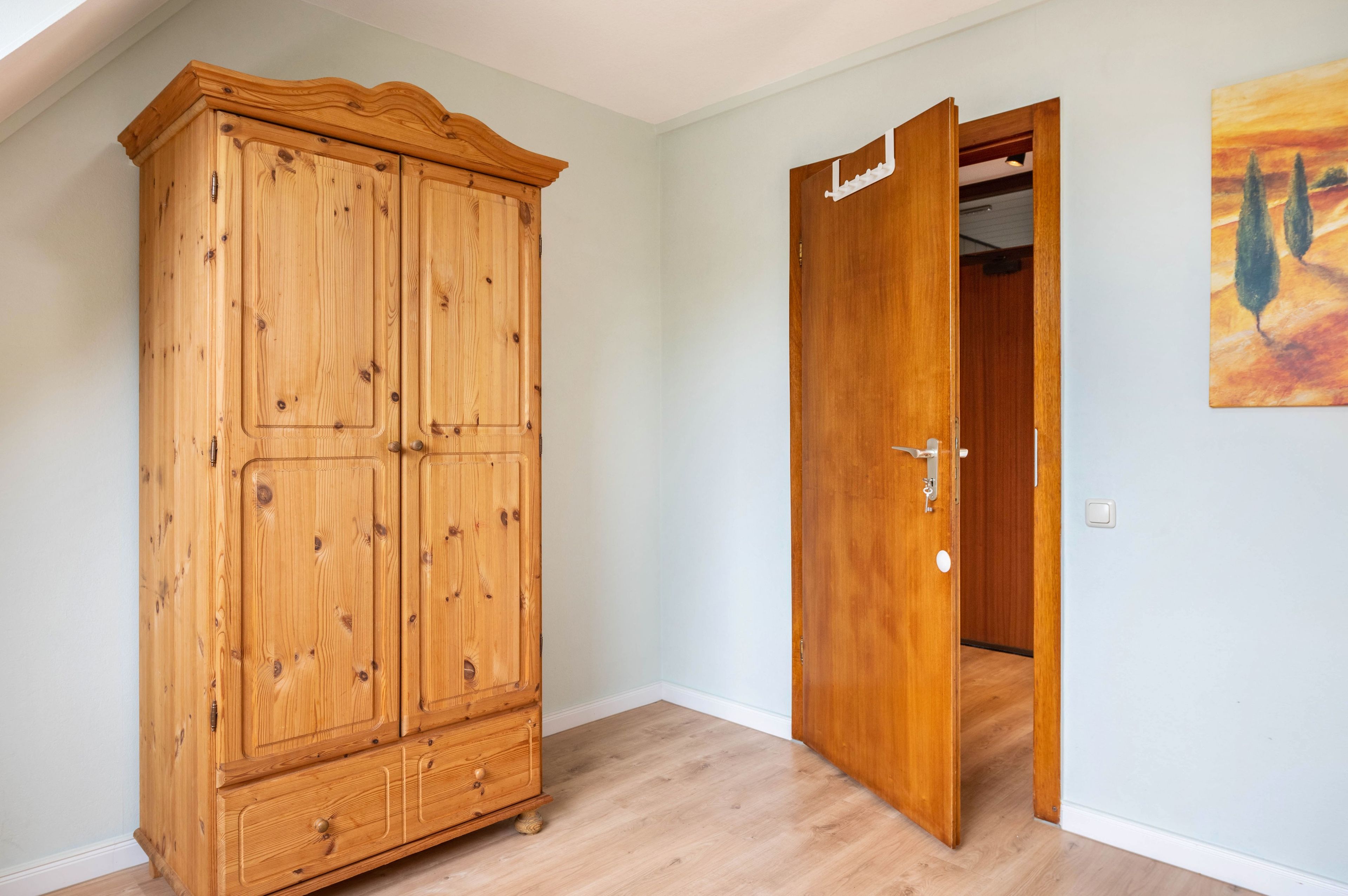 A room with a wooden wardrobe and a door leading to another room.