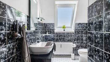 A modern bathroom with a freestanding bathtub, a toilet, and a window providing natural light.