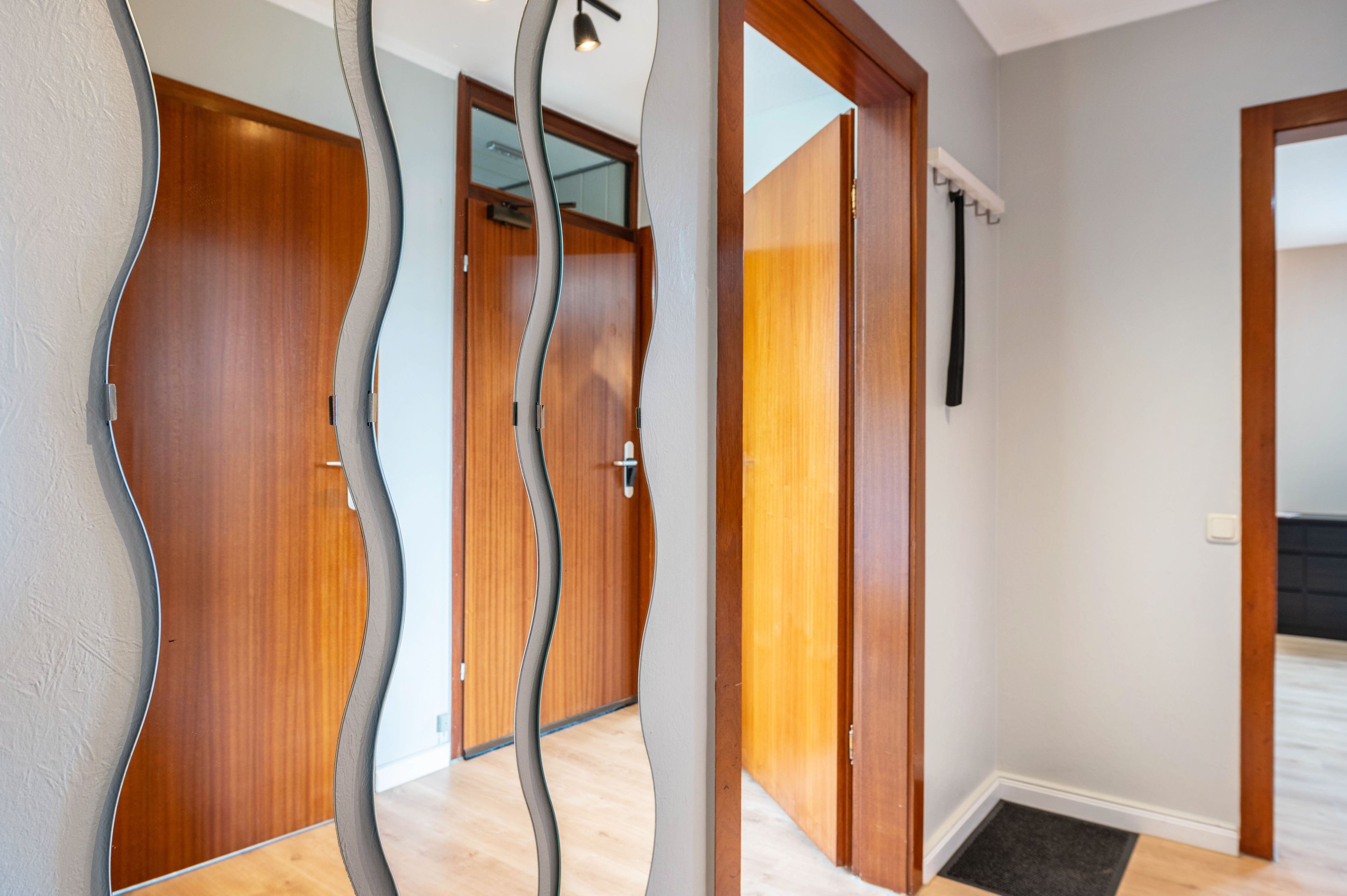 A hallway with wooden doors and a modern, wavy mirror.
