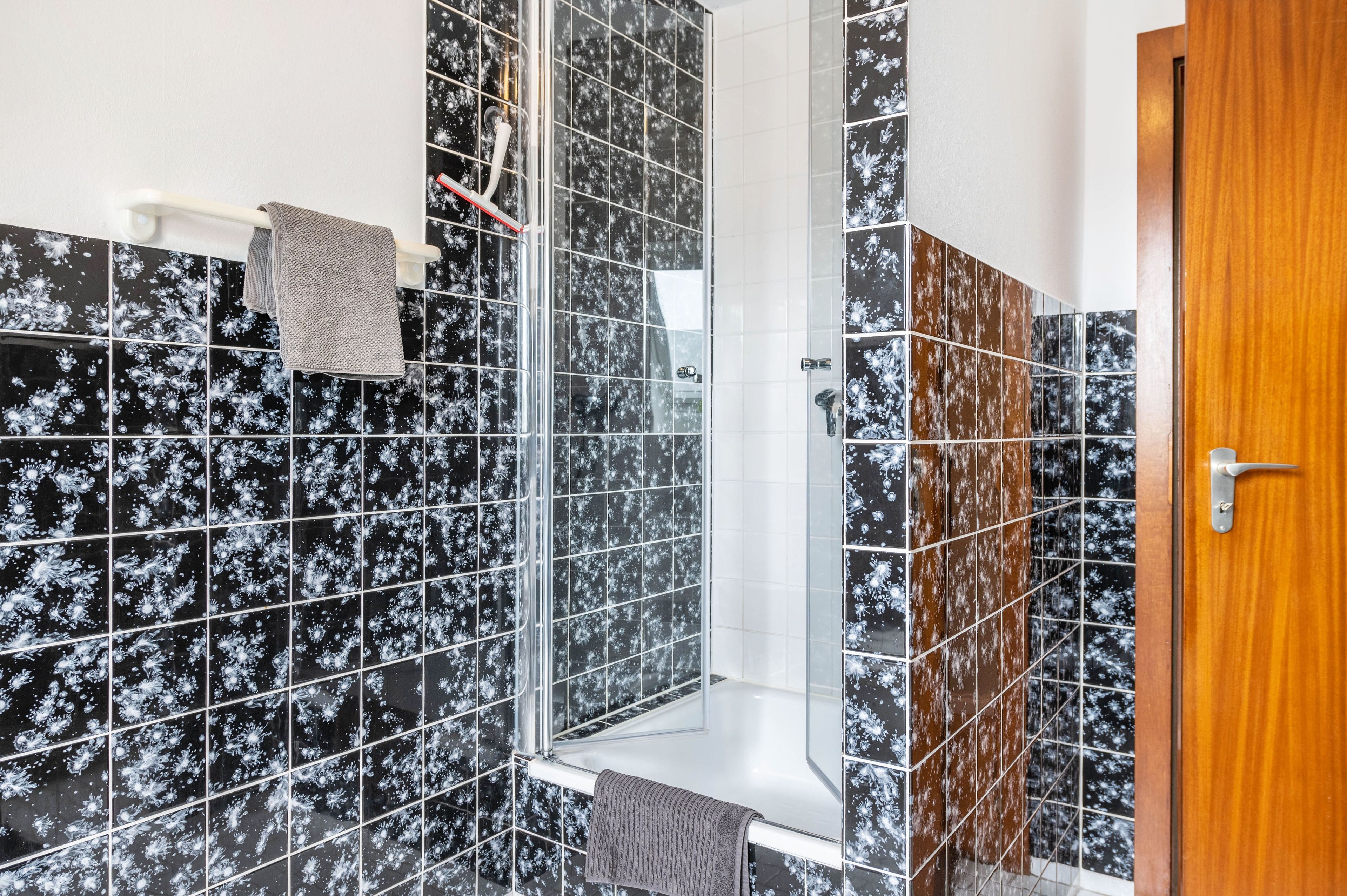 Un bagno con piastrelle a motivi bianchi e neri, box doccia in vetro e porta in legno.