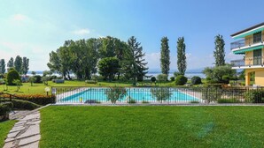 A swimming pool with a surrounding fence, lush green lawn, and a view of the sea. - Sporting A12 by Wonderful Italy (Sirmione)