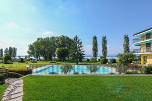 Piscina con valla perimetral, césped verde exuberante y vista al mar.