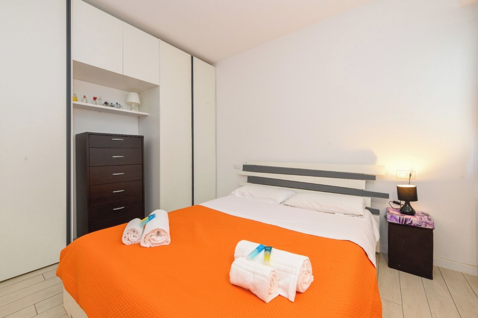 Een hotelkamer met een bed, een kledingkast, een nachtkastje en een plank met toiletartikelen.