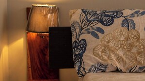 A neatly made bed with a blue and white floral bedspread, a wooden nightstand with a lamp, and a wall-mounted shelf. - Charming 2-bedroom Apartment in Bwebajja, Kampala (Entebbe)