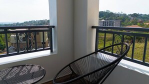 A balcony with a chair and a small table, overlooking a residential area with houses and greenery. - Charming 2-bedroom Apartment in Bwebajja, Kampala (Entebbe)