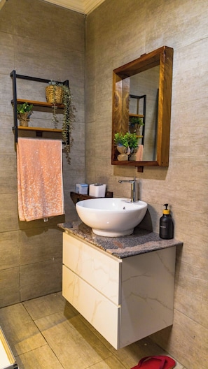 Ein Badezimmer mit einem weißen Waschbecken, einem Holzregal mit Pflanzen, einem Handtuch und einem Spiegel.
