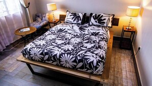 Een bed met een bloemenprint, twee bedlampen, een klein rond tafeltje en een stoel met kussen.