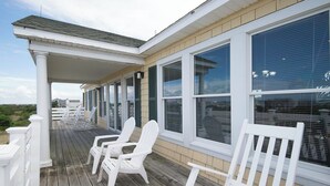 Una terraza de madera cubierta con sillas blancas y una valla blanca.
