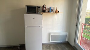 A compact kitchen with a refrigerator, microwave, and a small shelf with a coffee maker and other items. - Quiet, well-located studio apartment on the edge of the Garonne River (Toulouse)