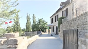 Un chemin de pierre mène à un bâtiment doté d’un portail en bois, d’un mur de pierre et d’une clôture en métal.