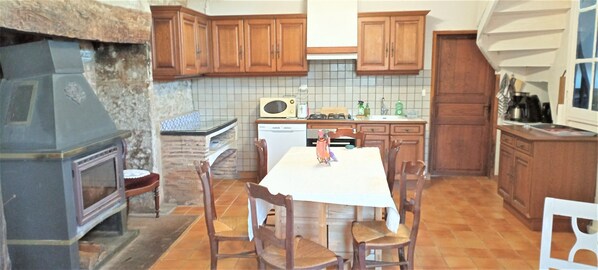 A kitchen with wooden cabinets, a stove, a microwave, and a dining table with chairs. - Stone House with Terrace, Garden, and Scenic Views (Séniergues)