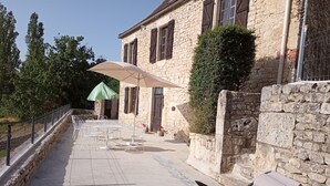 Un bâtiment en pierre doté d’une terrasse, d’une table et d’un parasol.