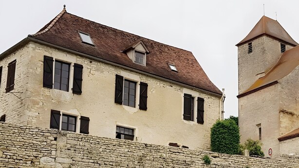 Un bâtiment historique doté d’un mur en pierre, d’une tour et d’une cour verdoyante.