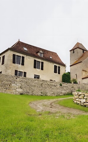 A historic building with a stone wall, a tower, and a grassy courtyard. - Stone House with Terrace, Garden, and Scenic Views (Séniergues)