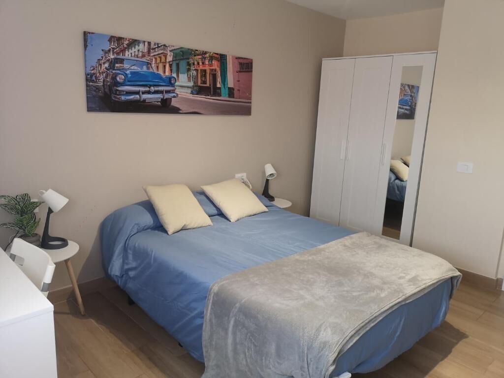 A bedroom with a bed, bedside tables, a lamp, a wardrobe, and a painting on the wall.