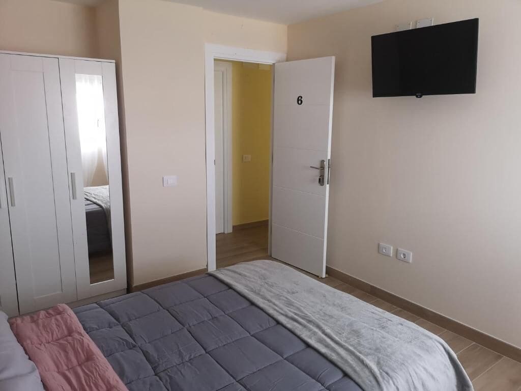Une chambre avec un lit, une armoire, une porte et un téléviseur fixé au mur.