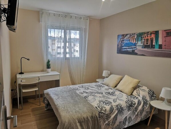 A bedroom with a bed, desk, chair, and a window with curtains. - Hostal Mari (San Cristobal de La Laguna)