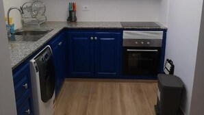 Uma cozinha compacta com armários superiores brancos, armários inferiores azuis, uma pia de aço inoxidável, uma máquina de lavar louça e um fogão.