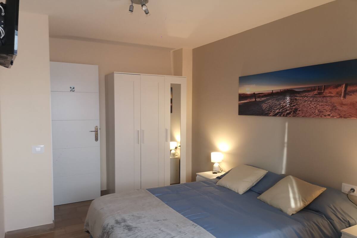 Een slaapkamer met een bed, nachtkastjes, een kledingkast en een schilderij aan de muur.