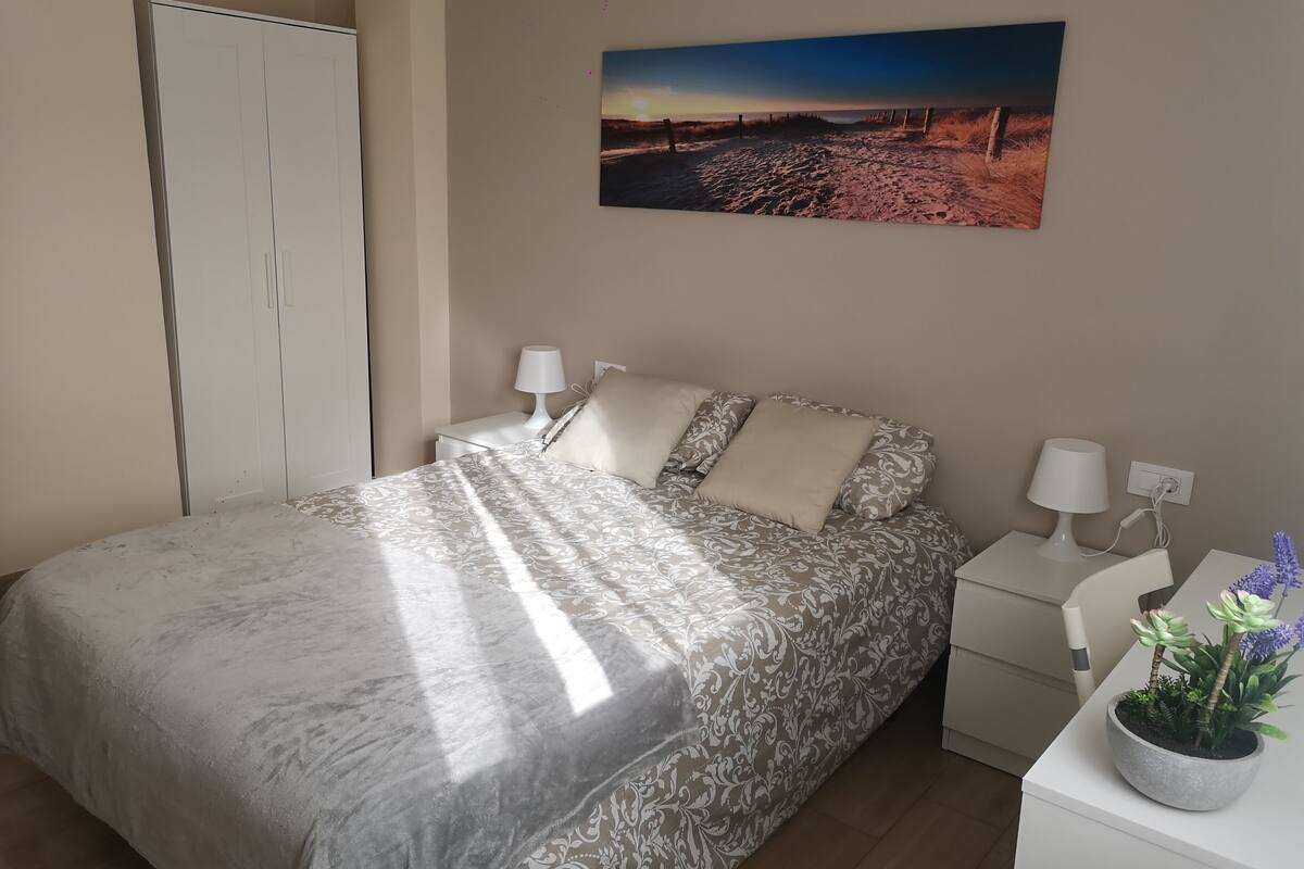 Een slaapkamer met een bed, twee nachtkastjes met lampen, een kledingkast en een aan de muur hangend schilderij.