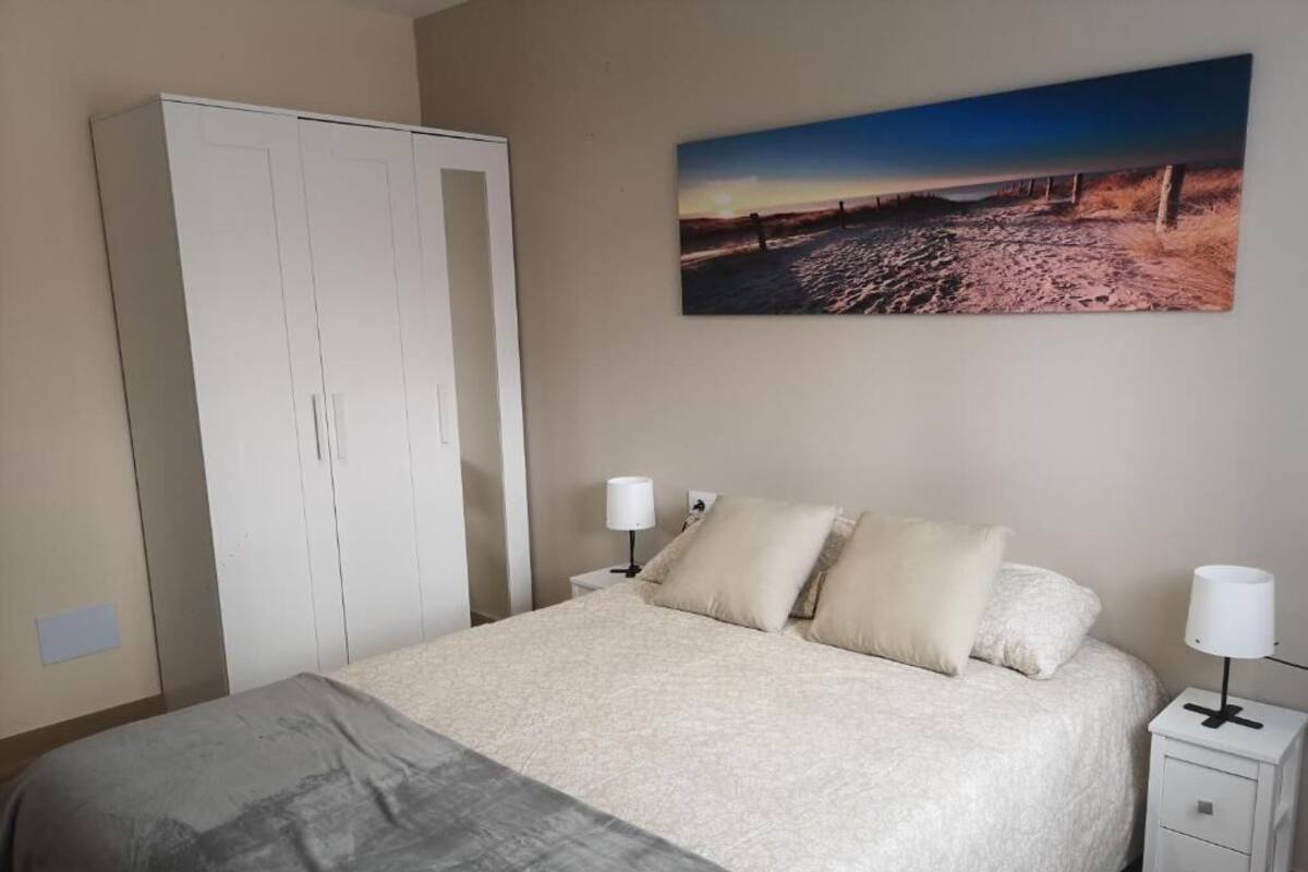 Een slaapkamer met een bed, twee nachtkastjes met lampen, een kledingkast en een schilderij aan de muur.