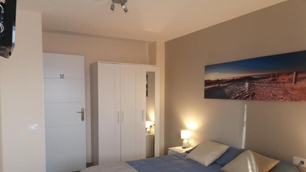 Quarto com cama, mesas de cabeceira, guarda-roupa e um quadro na parede.