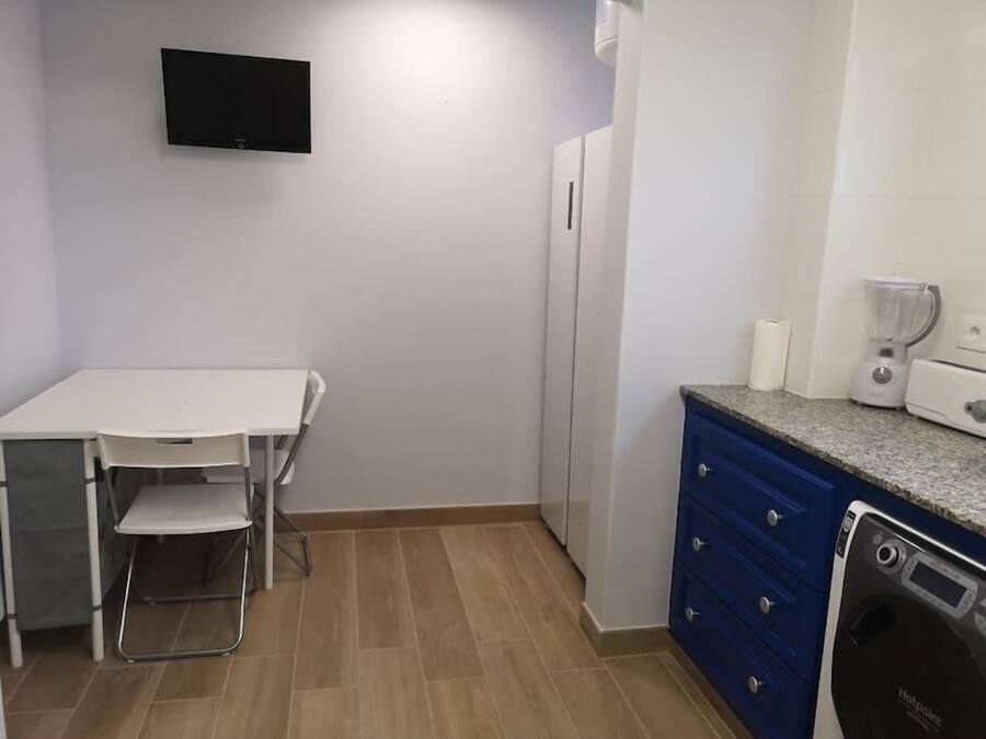 Una cocina compacta con una mesa blanca, un armario azul, un horno empotrado y un televisor montado en la pared.