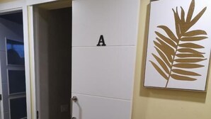 Quarto com porta deslizante marcada 'A', uma obra de arte com folha emoldurada na parede, e piso de madeira.