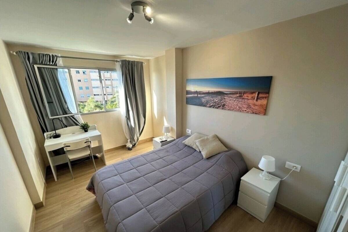 Een slaapkamer met een bed, een bureau, een stoel, een nachtkastje, een lamp en een schilderij aan de muur.