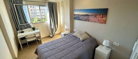 A bedroom with a bed, a desk, a chair, a nightstand, a lamp, and a painting on the wall.