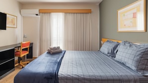 Hotellihuone, jossa on sänky, työpöytä, tuoli, televisio ja ikkuna, jossa on verhot.