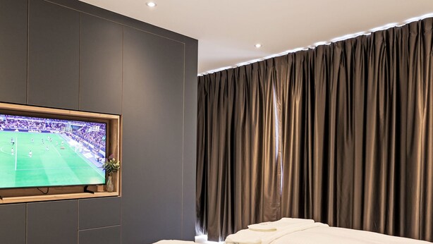 Ein Hotelzimmer mit einem Bett, einem an der Wand befestigten Fernseher und einem Vorhang.