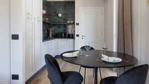 Una cucina moderna con mobili bianchi e una parete di fondo verde, che sfocia in zona pranzo con un tavolo rotondo e due sedie.
