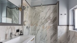 Un bagno moderno con una grande doccia in marmo, un lavandino bianco e uno specchio.