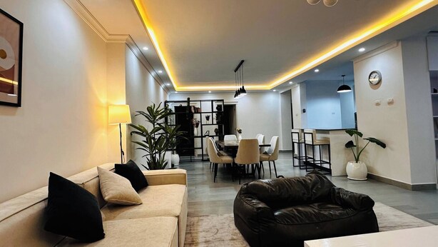 Una sala de estar moderna con un sofá, un sofá de cuero negro y una zona de comedor con una mesa y sillas.