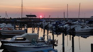 A marina with boats docked, a pier extending into the water, and a sunset in the background. - Waterfront holiday for multiple generations (Føllenslev)