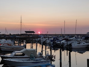 A marina with boats docked, a pier extending into the water, and a sunset in the background.