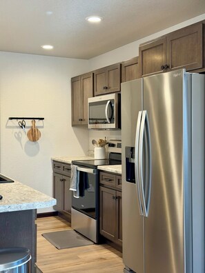 A modern kitchen with stainless steel appliances, wooden cabinets, and a marble countertop. - Ridge View Retreat! 2 bed, 2 bath with View and Garage (Rapid City)