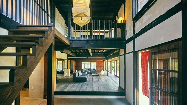 Un interior espacioso con una escalera de madera, una zona de estar central y grandes ventanales.