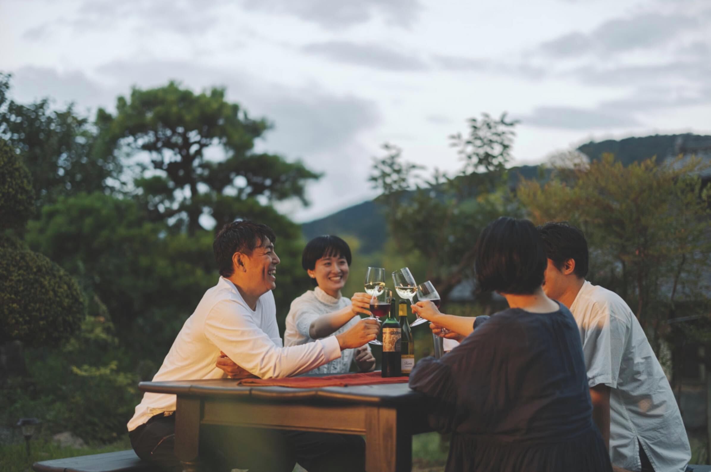 A group of people toasting with wine glasses at an outdoor table in a natural setting.
