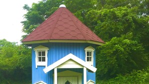 A small, blue, single-story house with a red roof, white trim, and a front door with a diamond-shaped window.